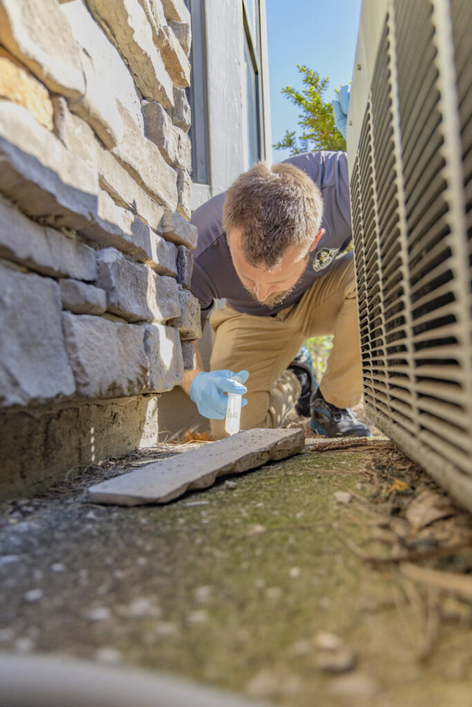 A Berner Pest Solutions technician in Lexington, KY, applying pest treatment near an outdoor AC unit.