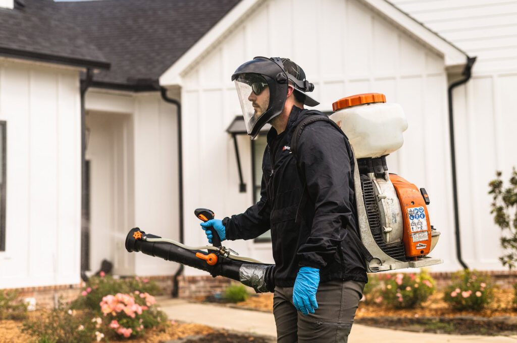 A pest control technician applying treatment to the exterior of a home for The Pest Detective in Cleveland, OH.