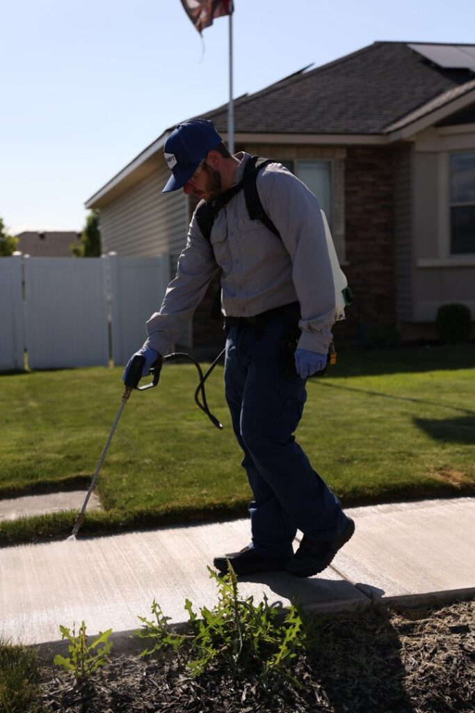 A Prompt Pest Solutions technician applying pest treatment to the ground near a house in Pocatello, ID.