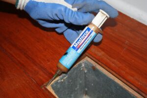 A Capital Pest Services technician applying roach killer bait gel into a floor vent in Raleigh, NC.