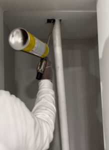 A pest control technician wearing gloves applying spray foam or sealant into a wall gap for pest exclusion by Bed Bug and Pest Removal LLC in Baltimore, MD.