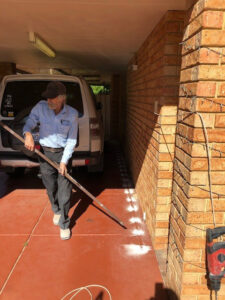 A Stewarts Pest Control Perth, WA technician applying a termite barrier treatment along the foundation of a brick building.