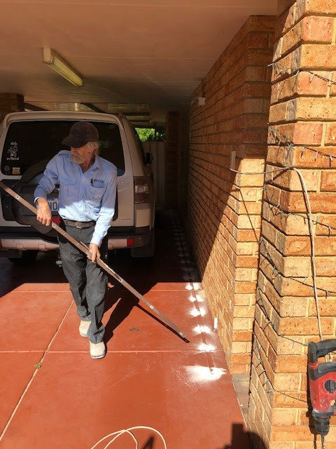 A Stewarts Pest Control Perth, WA technician applying a termite barrier treatment along the foundation of a brick building.