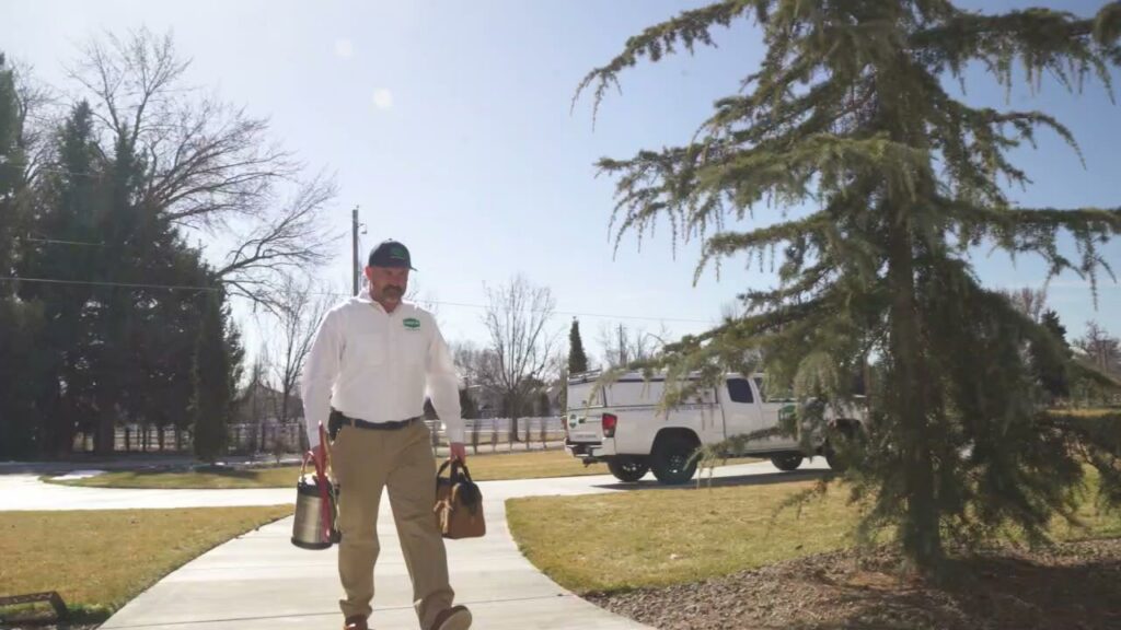 A Hemi Pest Control technician walking towards a home with pest control equipment for a service in Meridian, ID.