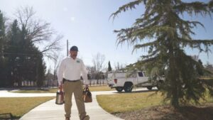 A Hemi Pest Control technician walking towards a home with pest control equipment for a service in Meridian, ID.