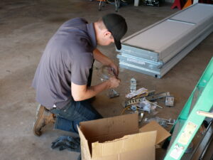 A Million Garage Door Services technician assembling new garage door parts on the floor, with panels stacked nearby in Colorado Springs, CO.