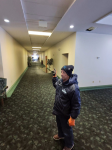 A John's Pro-Clean Carpet Cleaning technician assessing water damage on a wet carpet in a commercial hallway in Lansing, MI.