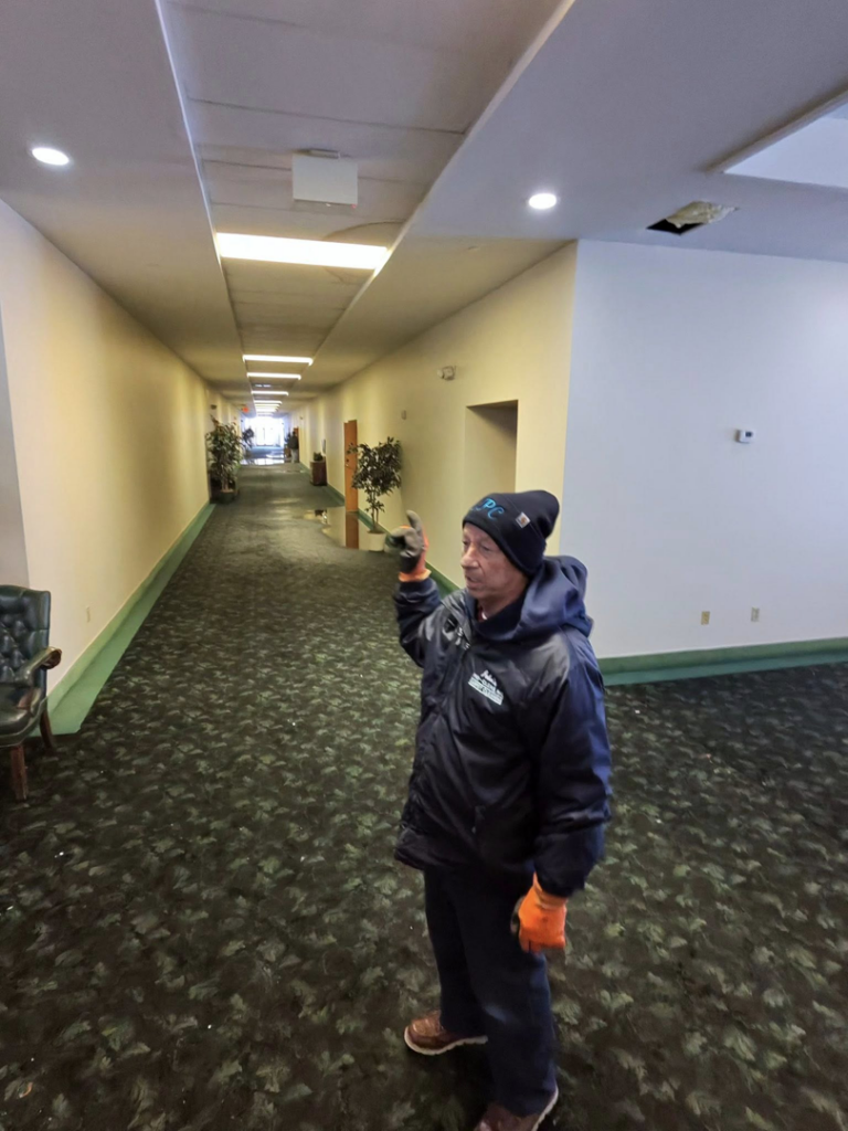 A John's Pro-Clean Carpet Cleaning technician assessing water damage on a wet carpet in a commercial hallway in Lansing, MI.