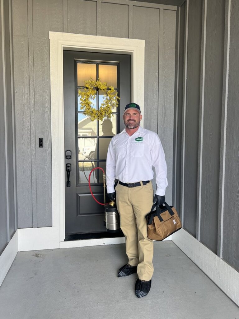 A Hemi Pest Control technician standing at a front door with a sprayer and tool bag, ready for service in Meridian, ID.