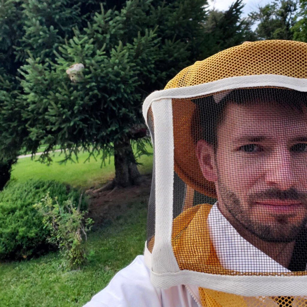 A SMART Exterminators technician in a protective beekeeper suit with a wasp nest visible in a tree, ready for pest removal in Cleveland, OH.