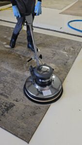 A technician in blue gloves operating a floor buffer to clean an area rug at Advanced Cleaning Systems in Atlanta, GA.