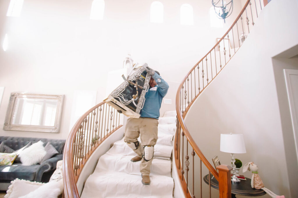 A technician carefully carrying an old furnace unit downstairs during a replacement for A/C Valley, LLC in Tempe, AZ.