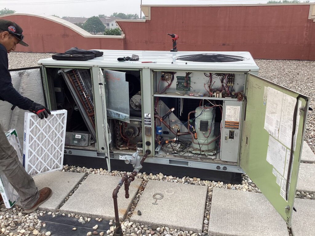 A technician changing an air filter in a large commercial rooftop HVAC unit for Service Champions Heating & Cooling in Aurora, IL.
