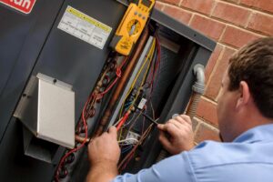 A technician checking electrical components inside an HVAC unit with a multimeter for Thomas Service Company in Huntsville, AL