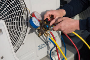 A technician checking refrigerant levels on an outdoor air conditioning unit with gauges for Adams Heating and Cooling in Schenectady, NY
