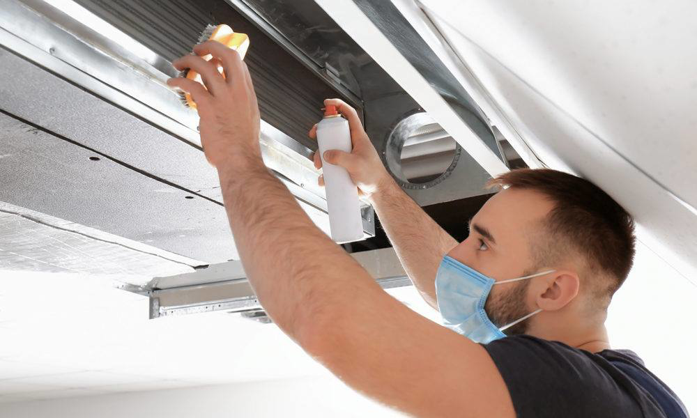 A technician in a mask cleaning an overhead air duct at Moss Creek HVAC Services in Colorado Springs, CO