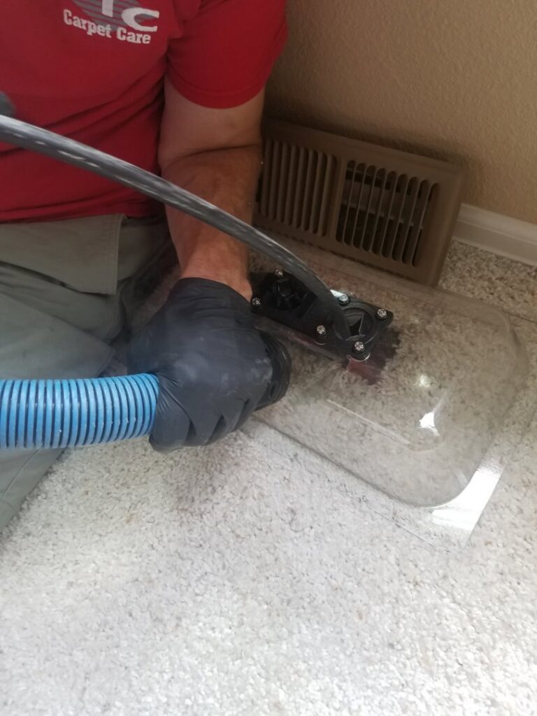 A technician's gloved hand operating a cleaning tool for an air duct on a carpeted floor by STC Carpet Care in Arvada, CO