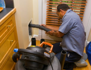 An Air Doctor Duct Cleaning & Lining technician cleaning an air duct opening with a powerful vacuum in Tulsa, OK.