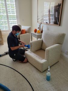 A masked technician performing upholstery cleaning on an armchair for Pacific Steam Carpet Cleaning in Gresham, OR.