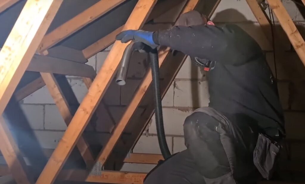 A pest control technician cleaning an attic, removing pest waste and insulation, for Rodent Control Cleveland in Cleveland, OH.