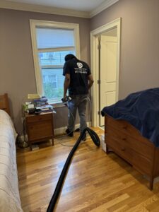 A technician from Boston Air Ducts Cleaning cleaning a floor air vent in a bedroom in Newton, MA.