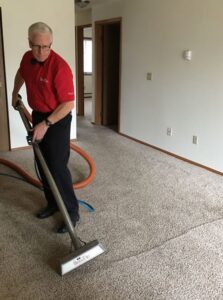 A BowTie Carpet Cleaning technician cleaning a light brown carpet in Appleton, WI, showing clean and dirty sections