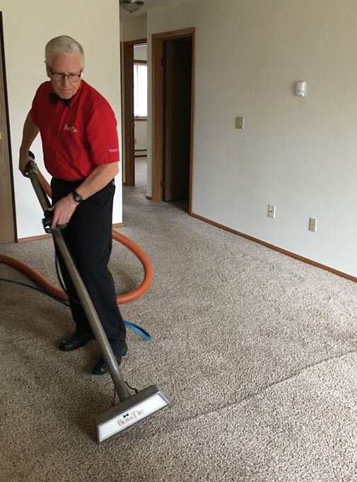 A BowTie Carpet Cleaning technician cleaning a light brown carpet in Appleton, WI, showing clean and dirty sections