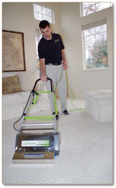 A professional technician operating a carpet cleaning machine on a light-colored carpet in a living room for Bee's Dry Organic Carpet Cleaning in San Antonio, TX.