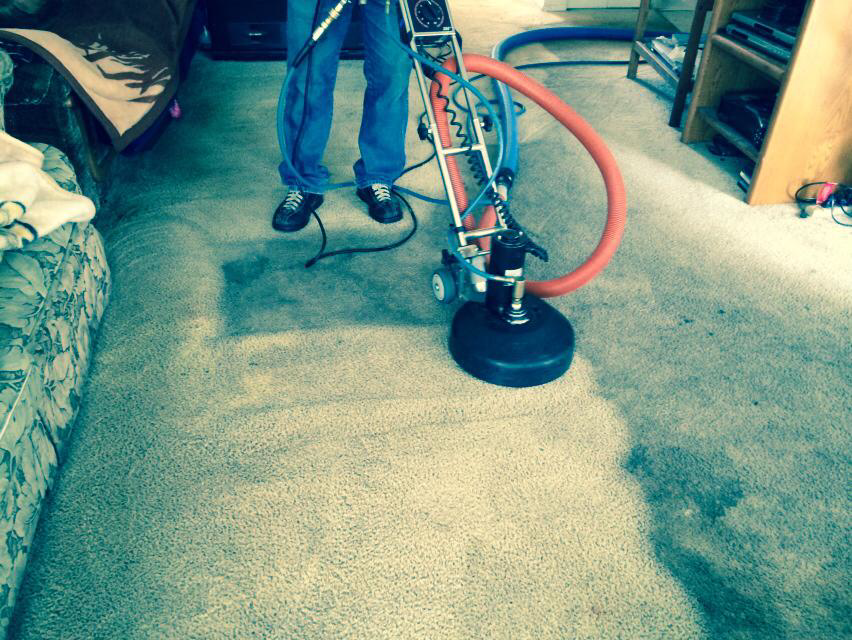 A technician operating a professional carpet cleaning machine on a light-colored carpet at Saras Clean Carpet in Portland, OR.