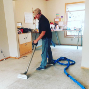 A technician professionally cleaning a carpet with a cleaning wand and hose for Green Planet Carpet Cleaning in Bloomington, MN.