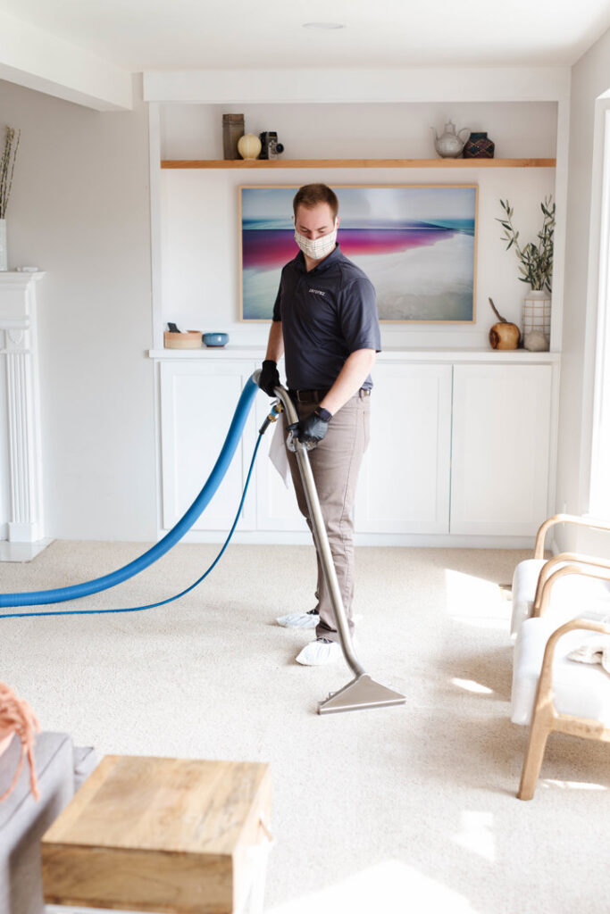 A Zerorez Greenville, SC technician in a mask cleaning a light-colored carpet with a professional cleaning wand.