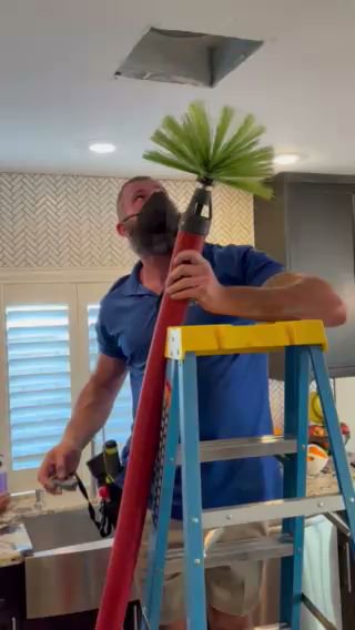 A Duct Dudes technician on a ladder cleaning a ceiling air vent with a specialized brush tool in Scottsdale, AZ.