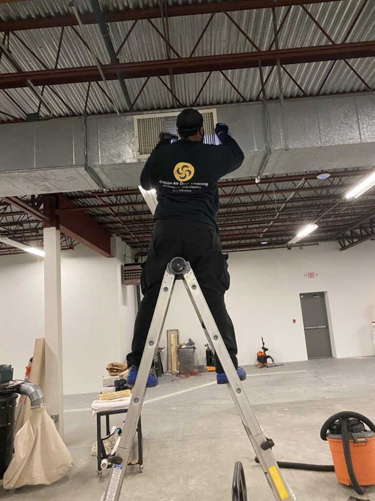 A technician from Boston Air Ducts Cleaning on a ladder, cleaning a ceiling air vent in Newton, MA.