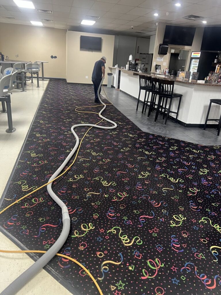 A technician using professional equipment to clean a vibrant, patterned commercial carpet at a business location by All-Star Carpet Cleaning in Dallas, TX.