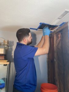 A Blue Bear Plumbing, Heating, & Air technician cleaning a ceiling duct vent in Norwell, MA.