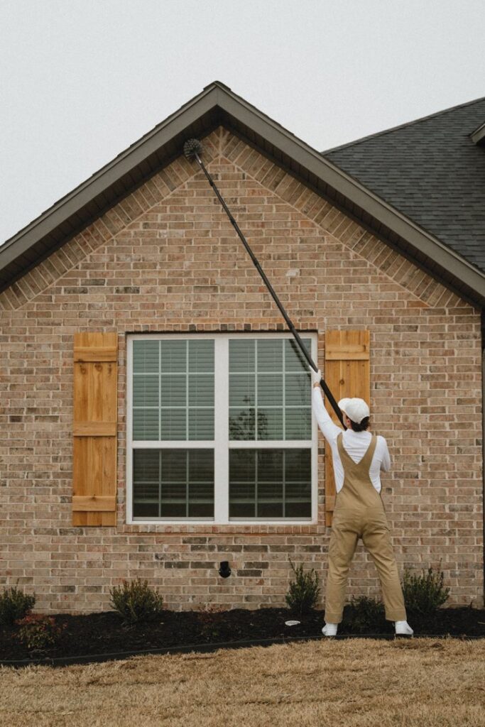 A Breezy Pest Control technician using a long pole to clean eaves for pest control in Little Rock, AR.