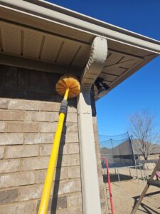 A technician from A Plus Pest Control using a long brush to clean eaves and gutters in Huntsville, AL.