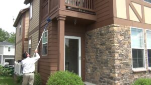 A technician cleaning the exterior of a house with a long pole for Springer Professional Home Services in Des Moines, IA.