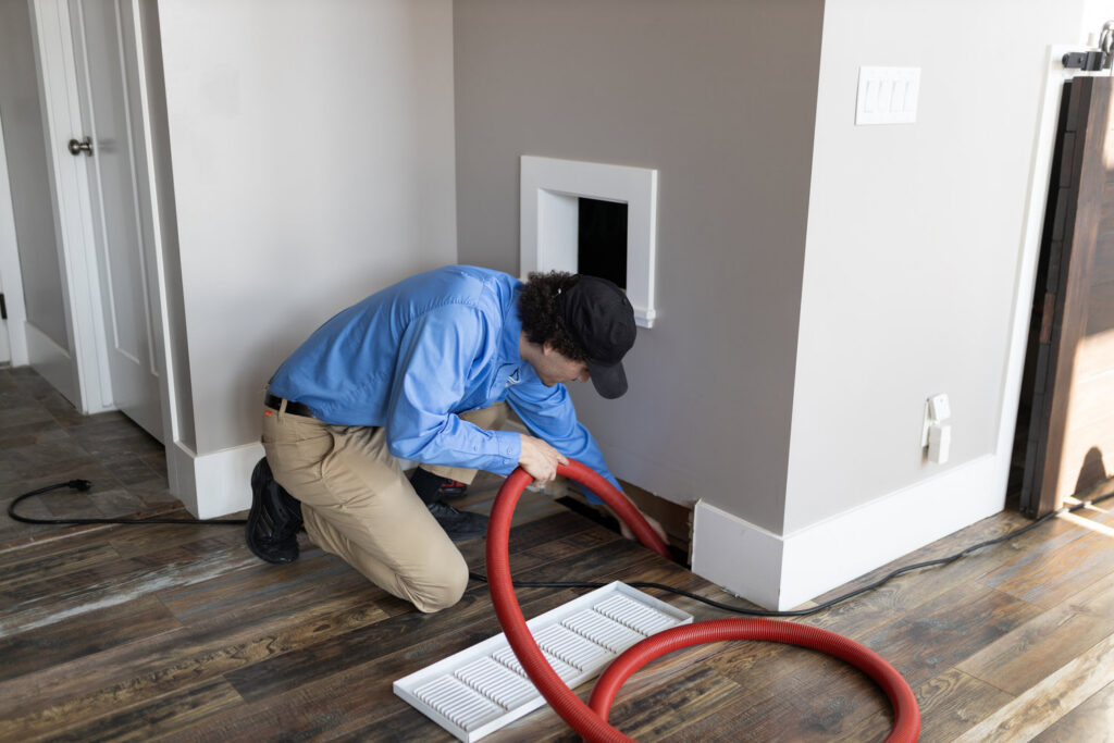An APEX Clean Air technician cleaning a floor air duct with a hose in a residential home in South Salt Lake, UT.