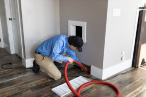 An APEX Clean Air technician cleaning a floor air duct with a hose in a residential home in South Salt Lake, UT.