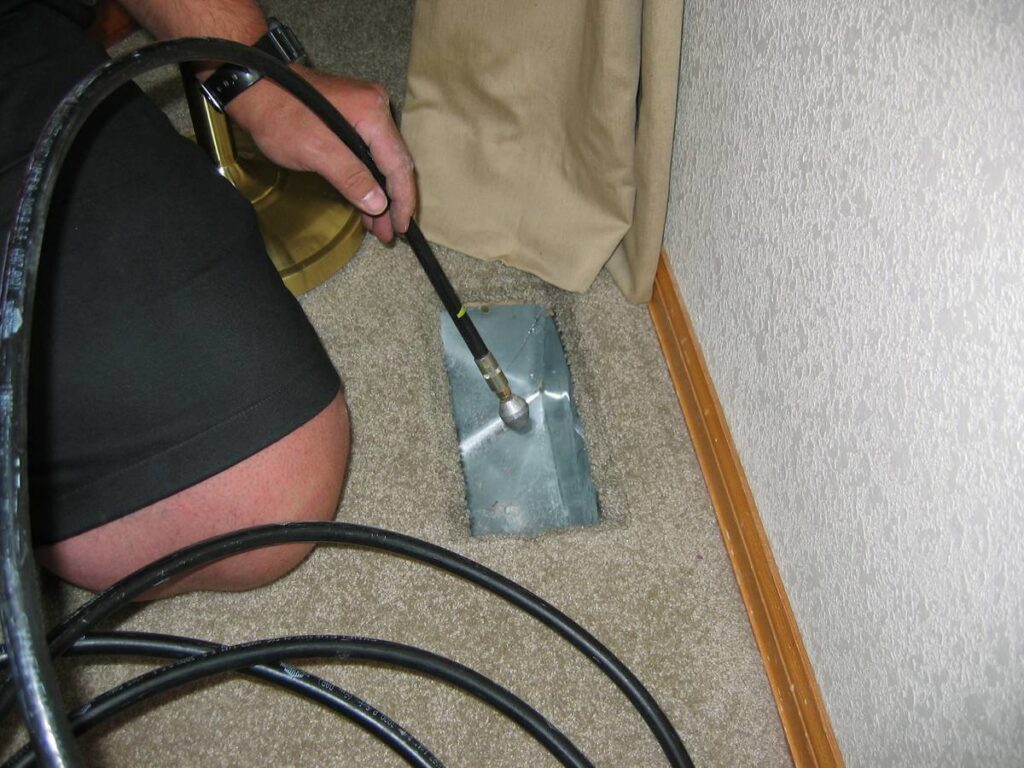 A technician using a specialized cleaning tool to clean a floor air vent, demonstrating services by Fresh N Clean Duct Cleaning in Arvada, CO.