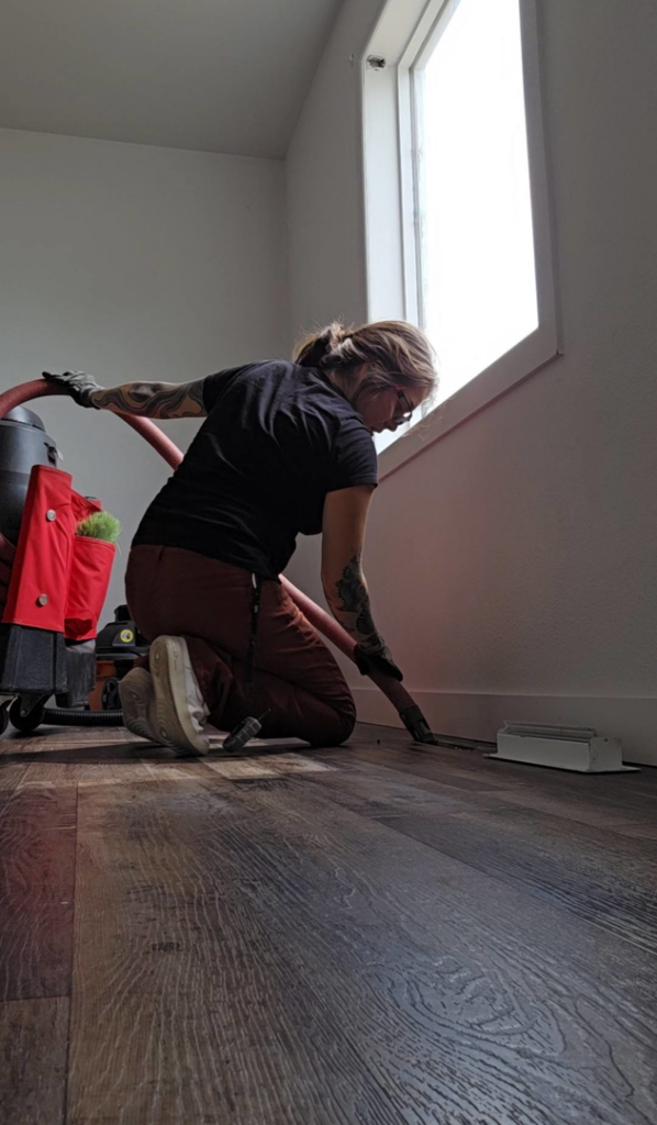 A technician cleaning a floor vent with a powerful vacuum system, performed by Aero Brush Duct Cleaning in Billings, MT.