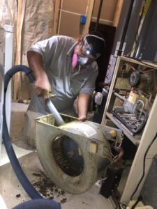 A Clean Air Solutions technician cleaning a dirty furnace blower motor and fan with a vacuum in Gaithersburg, MD.