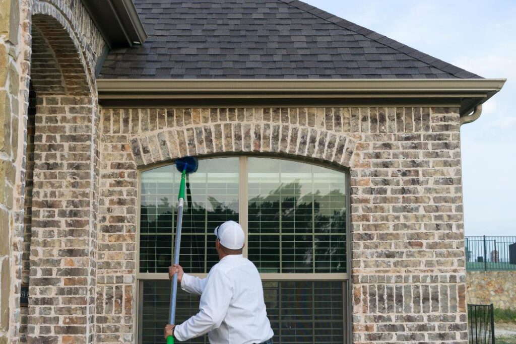 A Rumble Pest Solutions technician cleaning a house window during a pest control service in Springdale, AR.