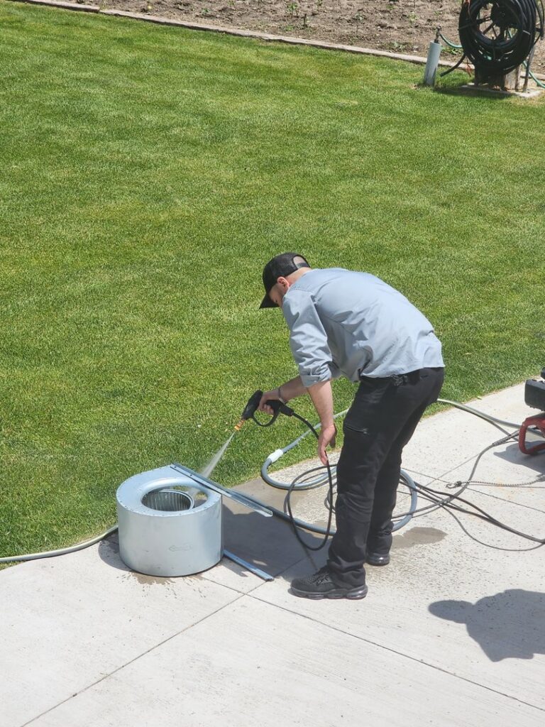 An APEX Clean Air technician pressure washing a removed HVAC blower fan outdoors in South Salt Lake, UT.