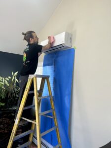 A Heat Pump Pros technician cleaning an indoor mini-split heat pump unit on a ladder in Hartford, CT.