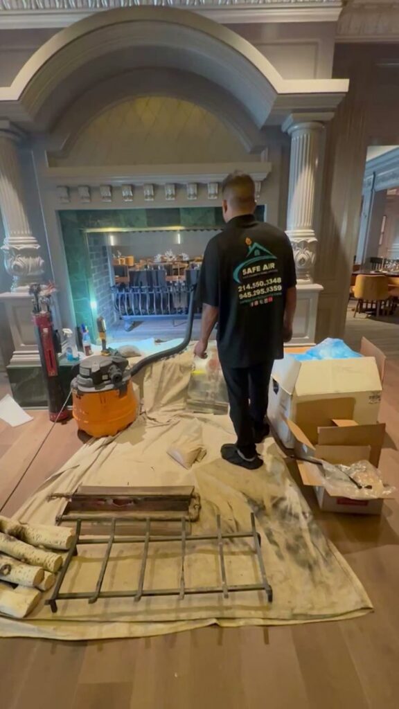A SafeAir Duct & Chimney technician cleaning a large, ornate fireplace during a chimney sweep service in Dallas, TX.