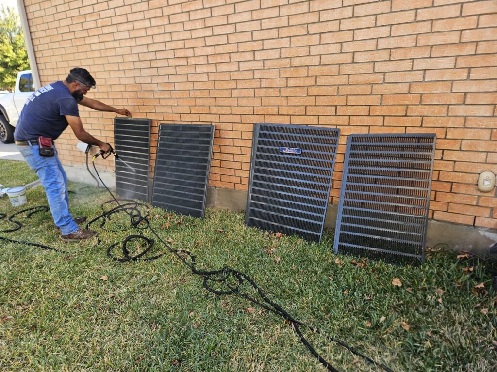 A Goettl Austin technician cleaning outdoor AC condenser coils during maintenance in Austin, TX