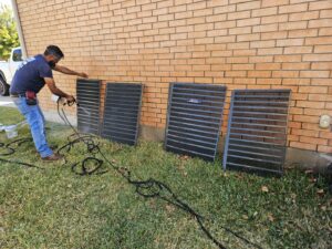 A Goettl Austin technician cleaning outdoor AC condenser coils during maintenance in Austin, TX