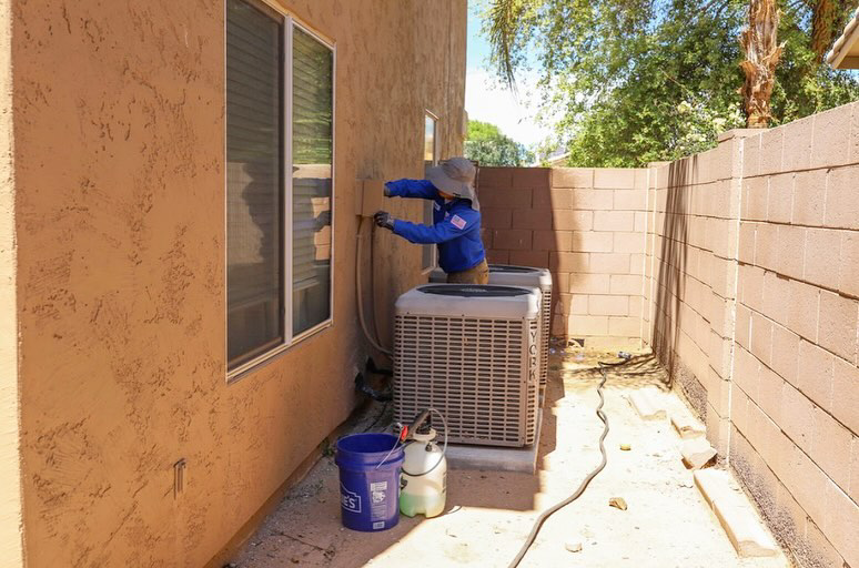A technician cleaning an outdoor AC unit with a hose for A/C Valley, LLC in Tempe, AZ.